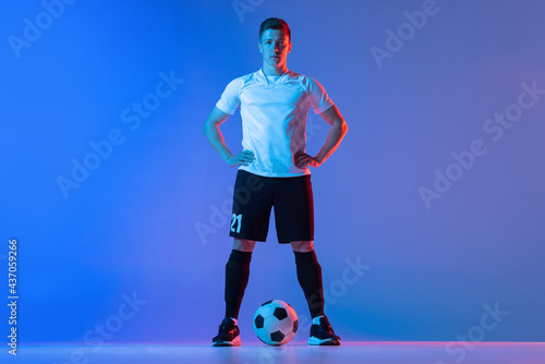 Fototapeta Naklejka Na Ścianę i Meble -  Full-length portrait of professional football player standing isolated on gradient blue pink background in neon light. Concept of sport, beauty.