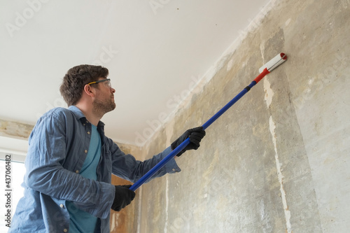 Caucasian man painting cement walls using roller brush and primer making a renovation. photo
