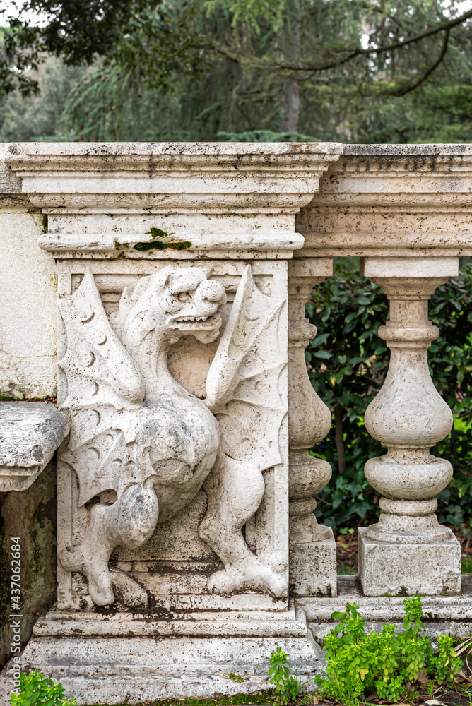 Detail of decorative marble sculpture of a dragon carved on and old handrail inside a park in Rome