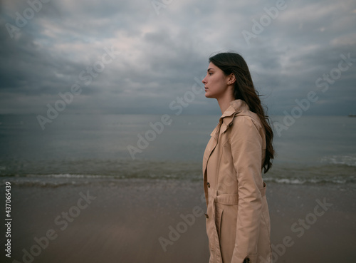 Lonely woman walks on the beach. Clothed brunette walking by seaside on the evening. One girl during spring vacation by the sea.