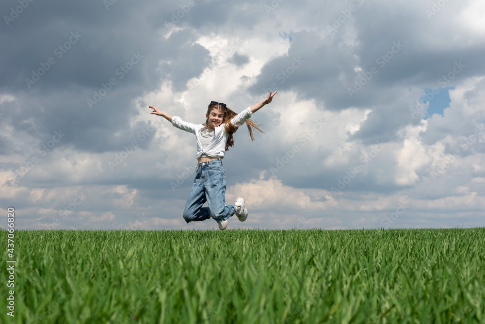 teen girl jumping in the green grass field, against the backdrop of the cloudy sky teen girl jumping in the green grass field, against the backdrop of the cloudy sky