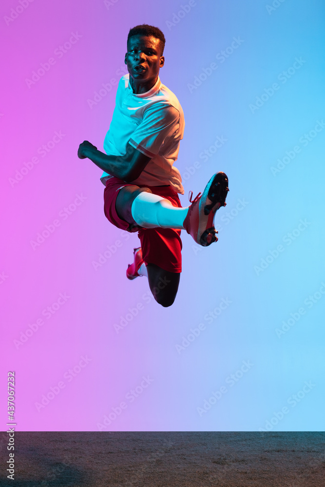 Obraz premium One African man, professional soccer football player training isolated on gradient blue pink background in neon light. Front view