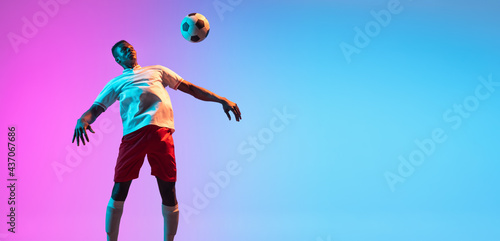 Flyer. One African man, professional soccer football player training isolated on gradient blue pink background in neon light. © master1305