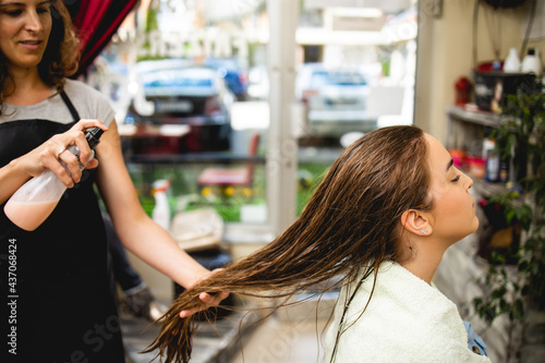 Hairdresser drying hair of a beautiful young adult woman in hair salon.