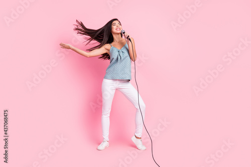 Full length photo of cheerful nice young woman sing stage good mood fly hair isolated on pink color background