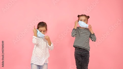 Two little girls put on medical masks. The sister helps the younger girl put on her mask. Prevention of infection with coronavirus infection.