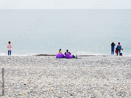 People stand by the sea and sit in armchairs on a cool spring day photo