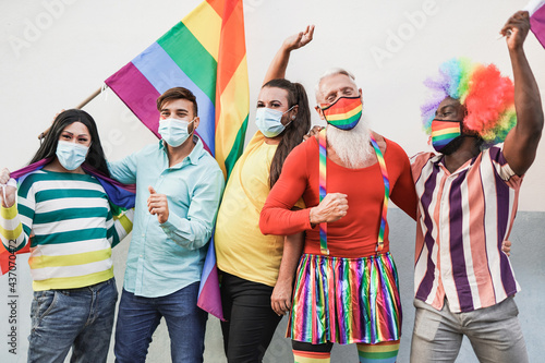 Happy gay men dancing at gay pride parade while wearing protective face mask for coronavirus - Homosexual and transgender concept - LGBTQIA