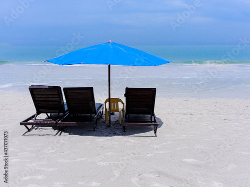 Three sunbeds and a blue umbrella on the beach with white sand on the beach