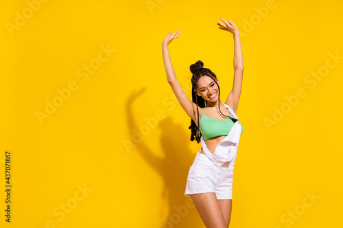 Photo of charming shiny dark skin lady wear green crop top smiling dancing rising arms isolated yellow color background