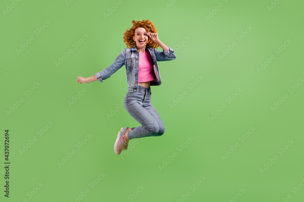 Full length photo of charming funny young lady dressed denim clothes glasses smiling jumping high isolated green color background