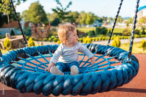 Cute little caucasian toddler swinging on the playground. Outdoor. Happy children's day