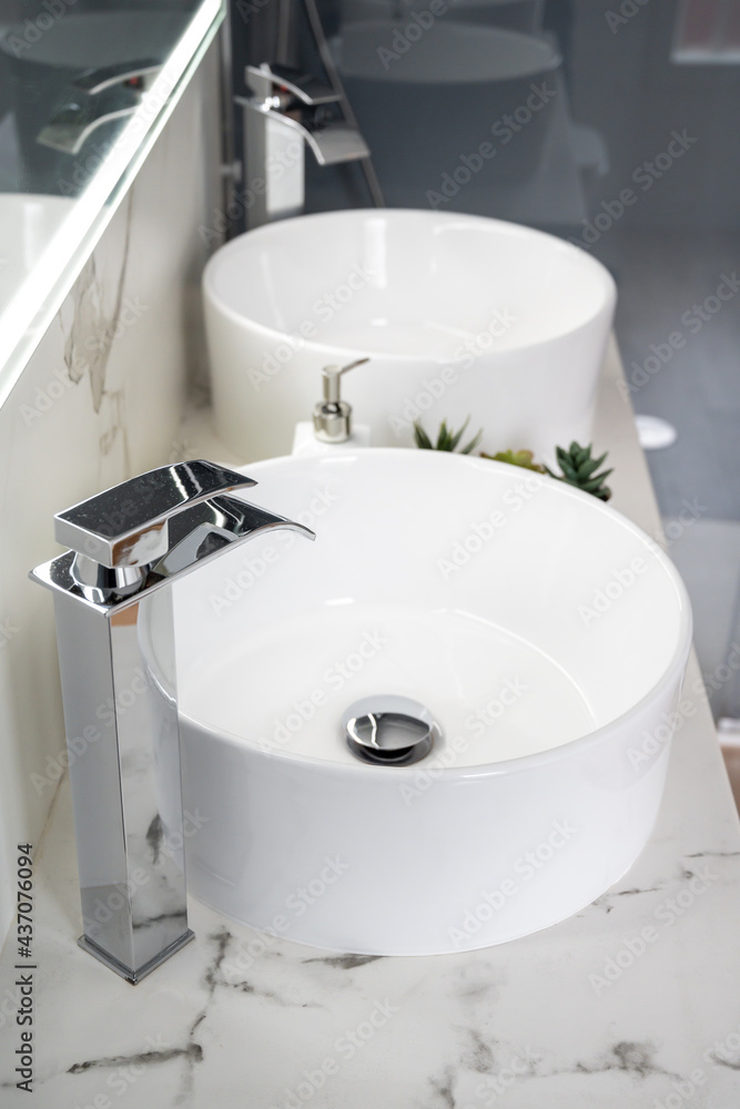 Fototapeta premium Pair of ceramic water basins in the interior of light modern bathroom with a mirror with light