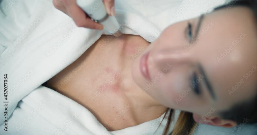 Close-up a female client in a bathrobe is laying in the cosmetology bed while having a non-injection bio-revitalization procedure by using the Dermadrop TDA device Close-up a female client in a bathrobe is laying in the cosmetology bed while having a non-injection bio-revitalization procedure by using the Dermadrop TDA device