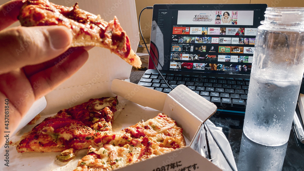 Foto Stock Amazonプライムビデオで映画やアニメ/ドラマを見ながらピザを食べます。デリバリーピザで食事。おうち時間/ステイホーム/コロナで変わる食生活と日常  | Adobe Stock