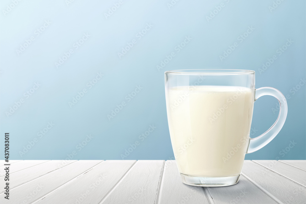 A glass mug of fresh milk on white wood with light blue background. A glass mug of fresh milk on white wood with light blue background.