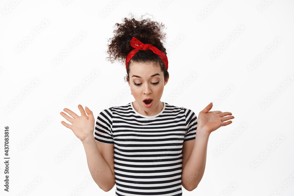 Startled brunette girl drop something, spread hands and looking down in awe, staring bellow at surprising thing, standing in t-shirt and headband against white background Startled brunette girl drop something, spread hands and looking down in awe, staring bellow at surprising thing, standing in t-shirt and headband against white background