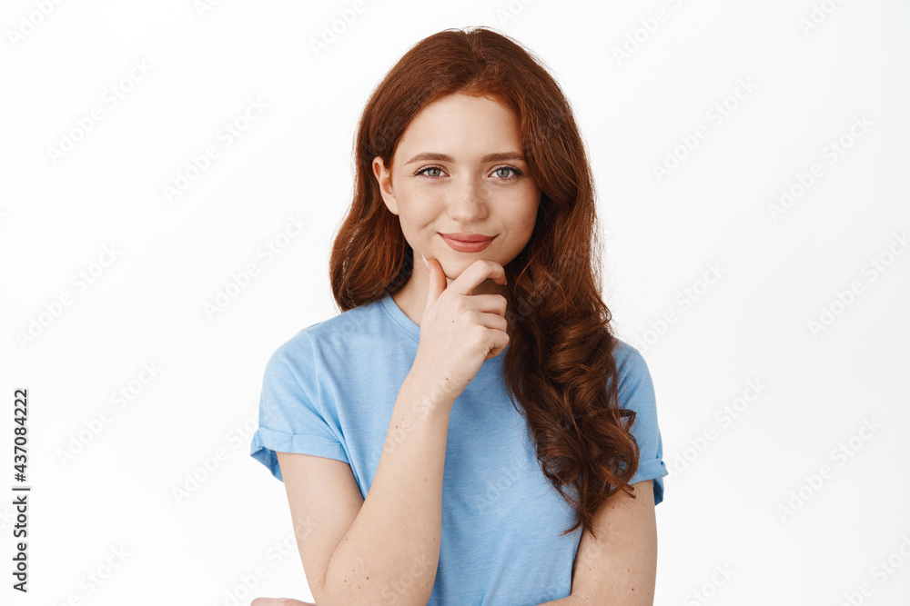 Hmm interesting. Thoughtful smiling woman with red hair thinking, touching chin and looking with interest, make decision, choosing, standing against white background and pondering Hmm interesting. Thoughtful smiling woman with red hair thinking, touching chin and looking with interest, make decision, choosing, standing against white background and pondering