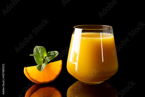 fresh orange juice into glass goblet on black background