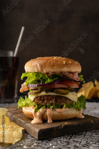 fast food. a large juicy burger with beef patty, iceberg lettuce, tomatoes, pickles, onions and sauce and bacon slices. Low key, dark mood