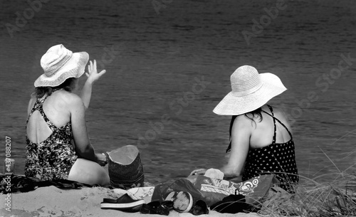 two women wearing hats at the beach watchiing their children