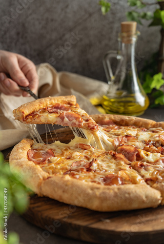 selective focus. hot pizza with cheese and pepperoni. the girl pulls a slice of pizza with melted cheese stretching. vertical position, dark mood