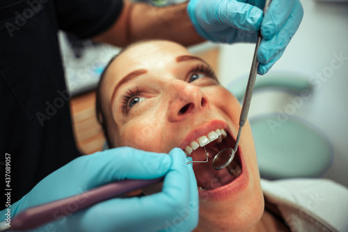 Caucasian female sitting on dentist chair getting teeth cleaned with tools 