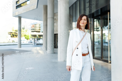 Beautiful middle age millennial stylish hipster woman posing outside, wearing white clothes. Success in Business district, copy space.