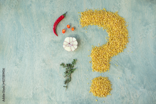 Fototapeta Naklejka Na Ścianę i Meble -  bulgur with spices on a green wooden background. beans of bulgur shaped like a question mark with chili, garlic and thyme.food composition or nutrition questions concept.copy space.Flat lay.