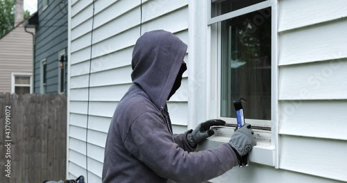 Burglar pries open a window with a crowbar and starts to climb into a home photo
