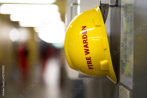 Fotografie A yellow safety helmet for Fire warden is hanging on wall in the building, standy by for use in fire emergency case