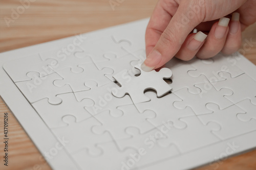 Young woman hand with long fingernails is placing white puzzle in last gap in the middle of the board to complete it. Wooden table background