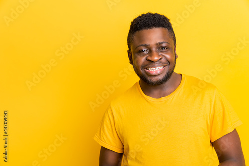 Head shot smiling african american millennial young man wearing trendy yellow t-shirt, looking at camera isolated on blank yellow studio background, handsome young black male guy posing for portrait