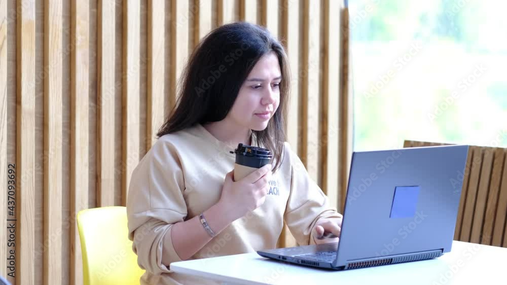 Young hipster woman sitting in coffee, drinking coffee and using laptop.On table is laptop. Girl browsing internet, chatting, blogging. Young hipster woman sitting in coffee, drinking coffee and using laptop.On table is laptop. Girl browsing internet, chatting, blogging.