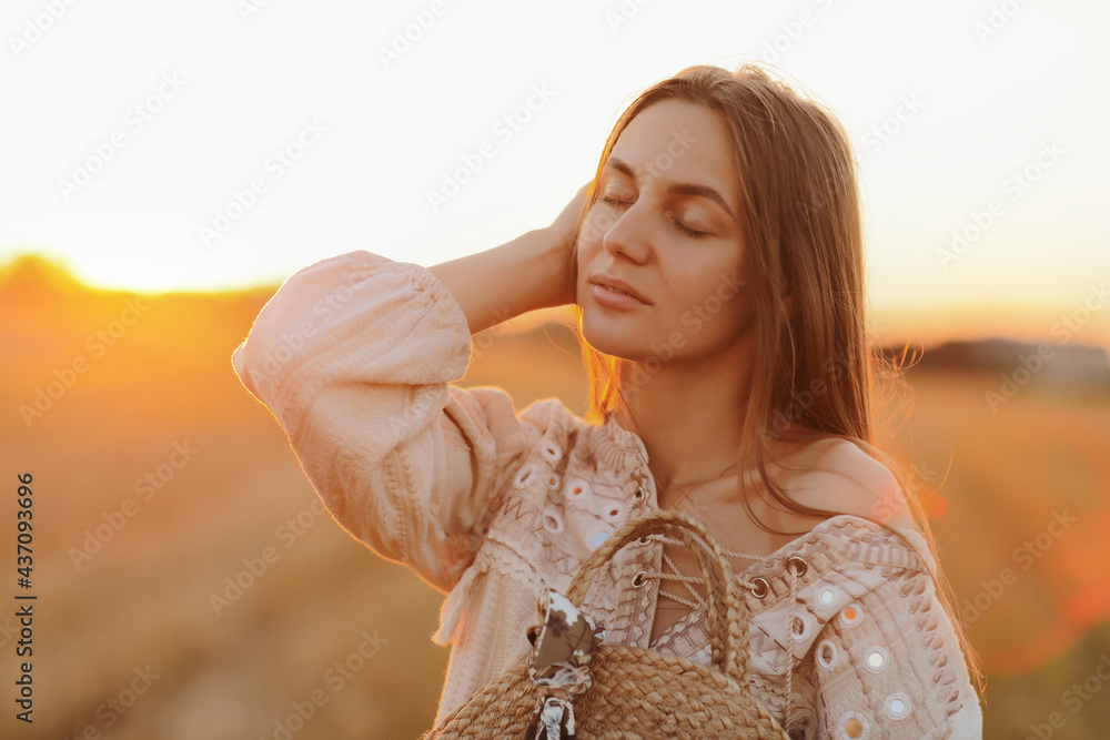 girl with long hair and straw bag in hand in the summer at sunset in the field for a walk. she is happy, her eyes are closed. background blurred art photography