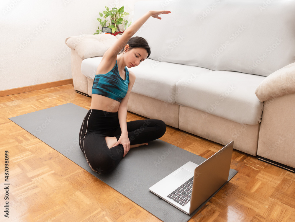 Woman stretching at home while looking at her laptop. Woman stretching at home while looking at her laptop.