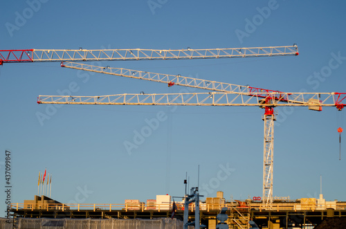 Red and white construction cranes on a building, against a blue sky