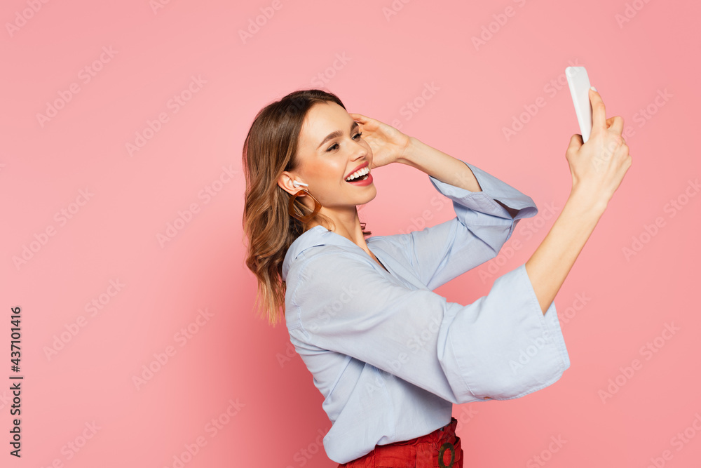 Positive woman in earphone having video call on cellphone on pink background Positive woman in earphone having video call on cellphone on pink background