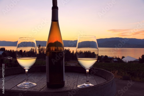 Dark sunset - romantic scene with the wine glasses and bottle of white wine on the wooden barrel by Okanagan Lake in Kelowna, BC