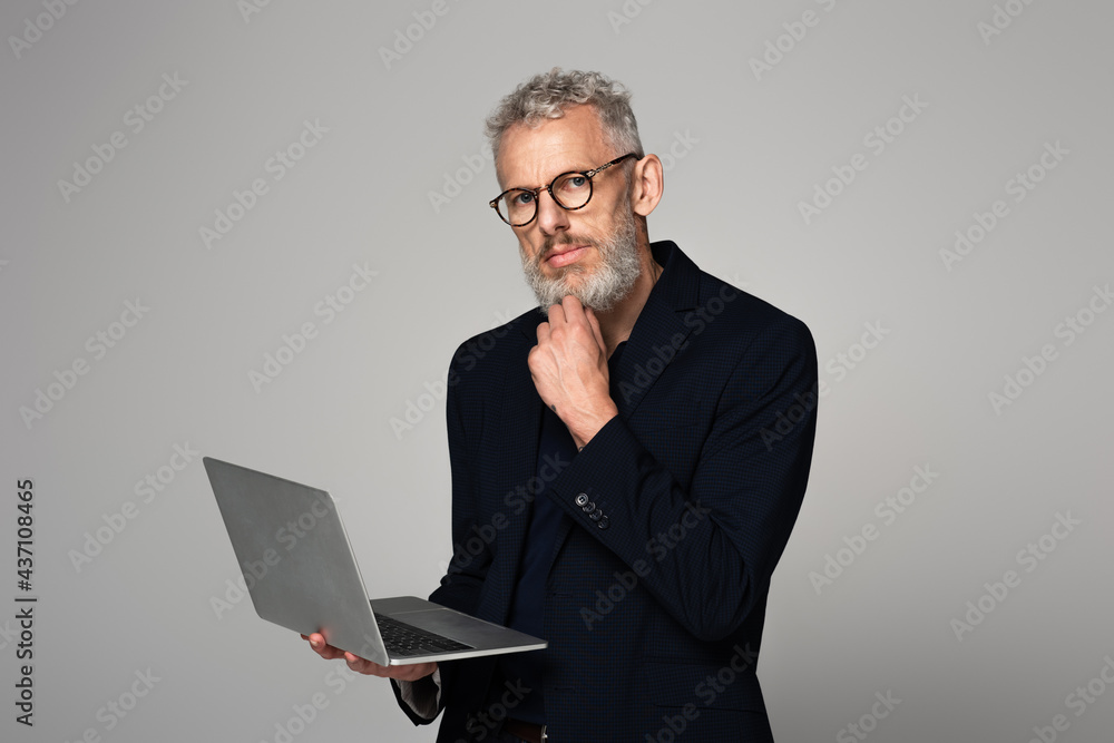 pensive middle aged man in glasses holding laptop isolated on grey pensive middle aged man in glasses holding laptop isolated on grey