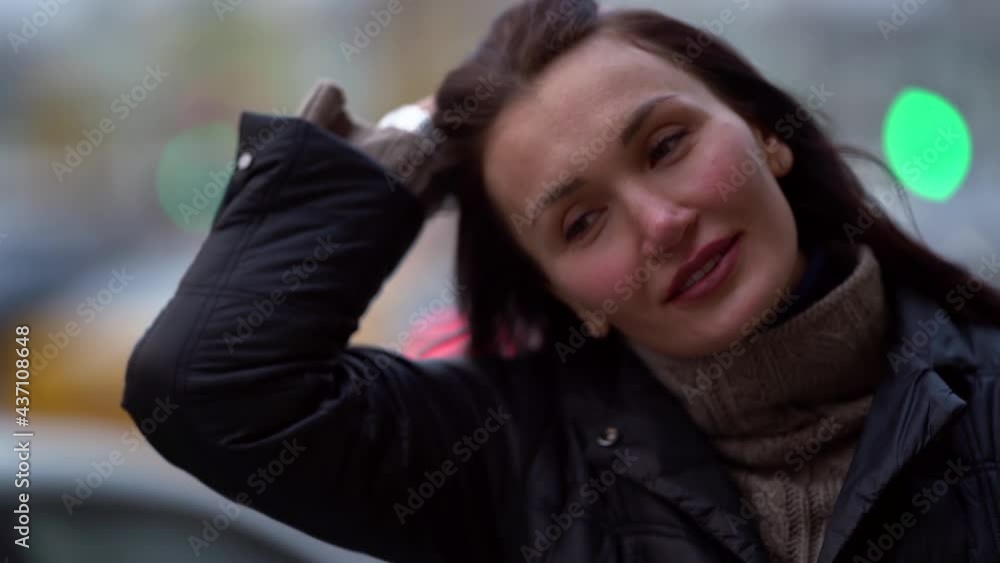 portrait of a brunette in a knitted sweater and a dark coat on a cloudy day. she straightens her hair against the out-of-focus street lights. close-up portrait of a brunette in a knitted sweater and a dark coat on a cloudy day. she straightens her hair against the out-of-focus street lights. close-up