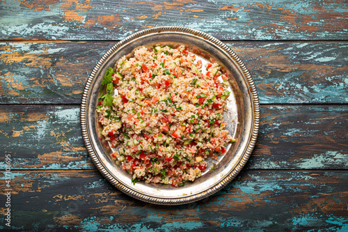 Middle eastern and Mediterranean traditional vegetable salad tabbouleh with couscous on rustic metal plate and wooden background from above. Arab Turkish food 