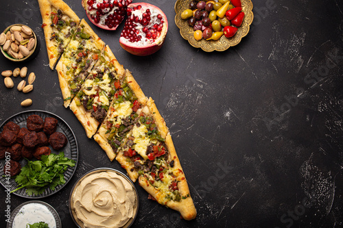 Various Turkish dishes: pide pizza, meat kebab with tabbouleh salad, falafel, hummus, olives and Middle Eastern meze on black table top view with copy space. Ethnic arab food, cuisine of Turkey
