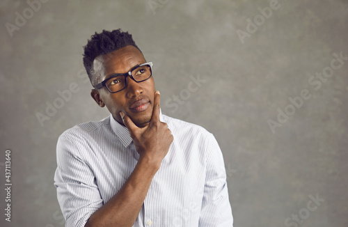 Black man in white office shirt and eyeglasses looks up thinking, wondering, taking decision. African American business manager with thoughtful face expression unsure, doubting, uncertain, hesitating