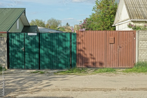 two closed private gates of green and brown metal on the street by the gray road © butus