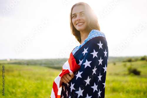 Young woman with american flag on blooming meadow. 4th of July. Independence Day. Patriotic holiday. USA flag fluttering in the wind.