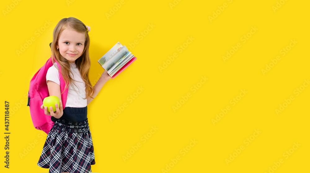 Back to school. Little blonde girl with school backpack. An elementary school student smiles and holds book and green apple on yellow background. Back to school. Little blonde girl with school backpack. An elementary school student smiles and holds book and green apple on yellow background.