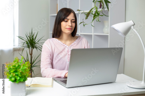 Portrait of a young beautiful woman working on a laptop at home. A Spanish girl student uses a computer to study remotely online.