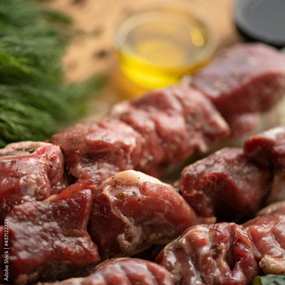 Raw meat is marinated for baking on skewers. Kebab preparatory and cooking Process. Sirloin, spices and greens on kitchen table. Blurred background. Close up shot. Soft focus. Square format.