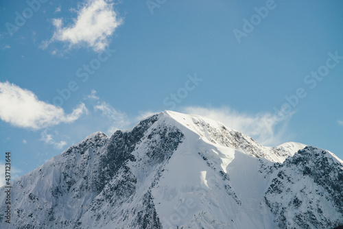 Great view to high snowy mountain peaked top with low cloud under cirrus clouds in sky. Low clouds on big snow covered mountains with sharp pinnacle in sunshine. White-snow pointy peak in sunlight.